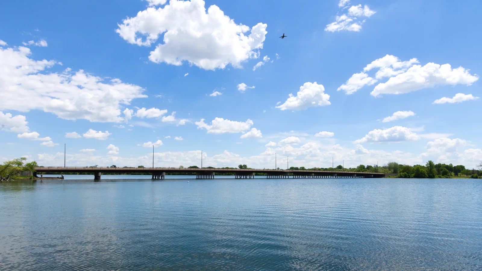 Lake Nokomis and the Cedar Avenue bridge under a bright blue sky with big summer clouds.