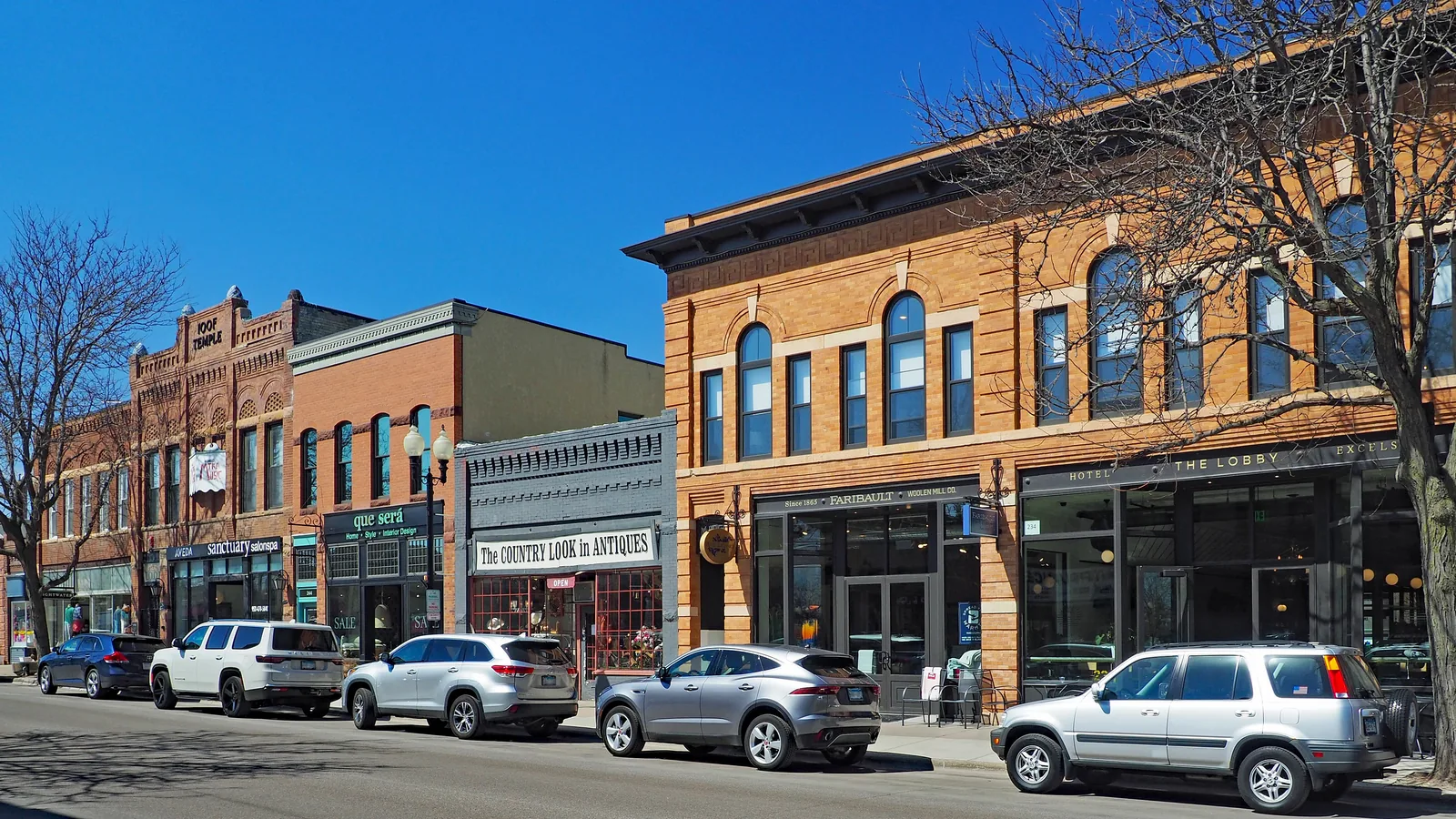 Water Street in downtown Excelsior under a clear blue sky, lined with historic brick storefronts including the IOOF Temple building and Hotel Excelsior.