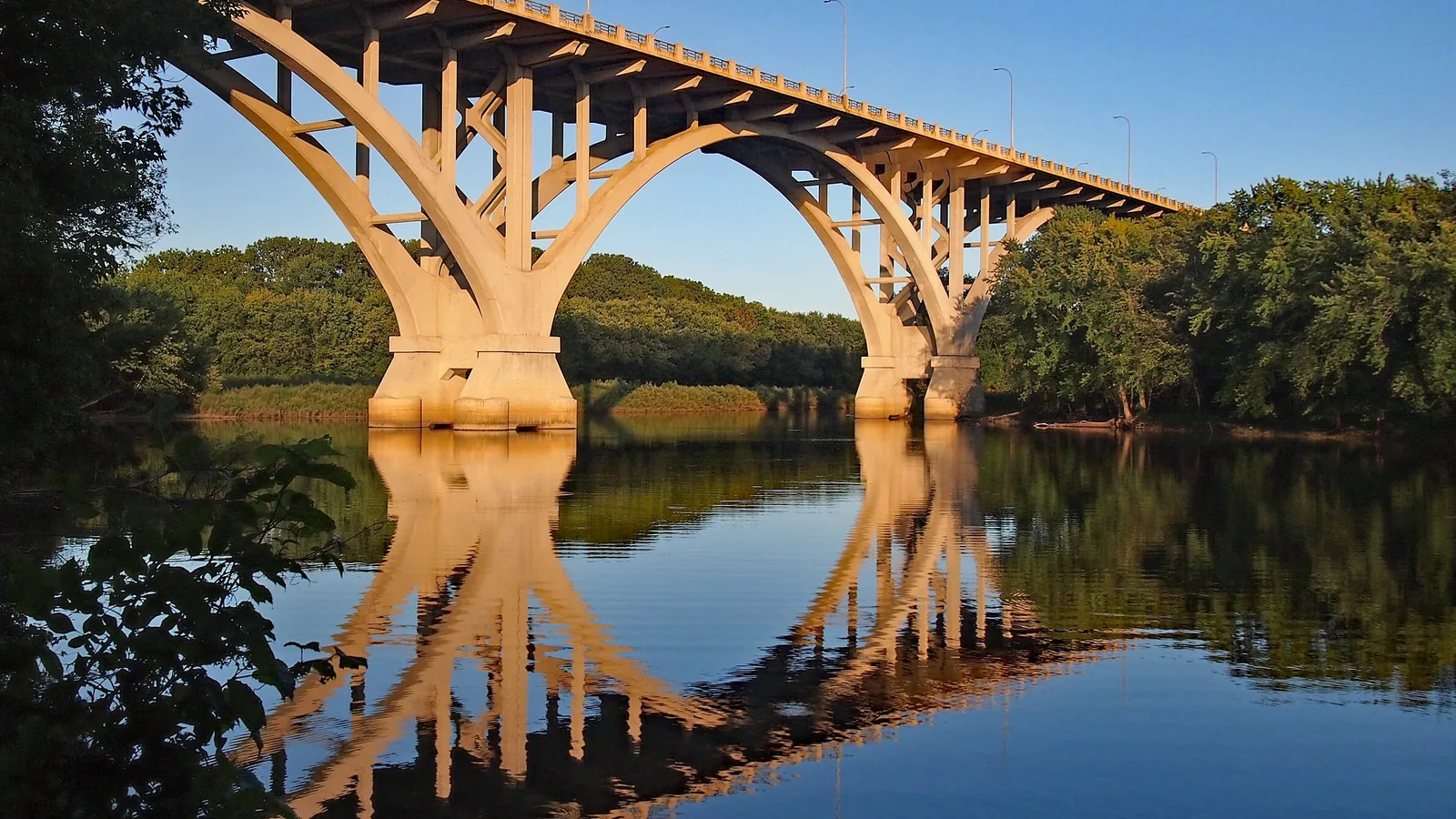 The arches of the Mendota Bridge lit by low sun and mirrored in the still water of the Minnesota River below Mendota Heights.